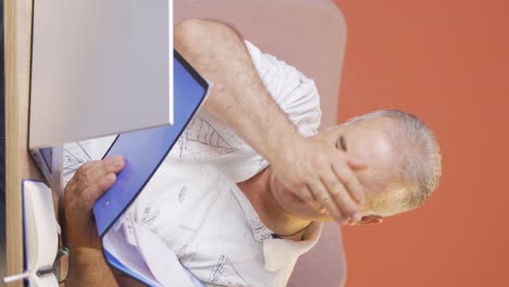 Vertical-video-of-Old-man-working-on-laptop-throws-files-angrily.